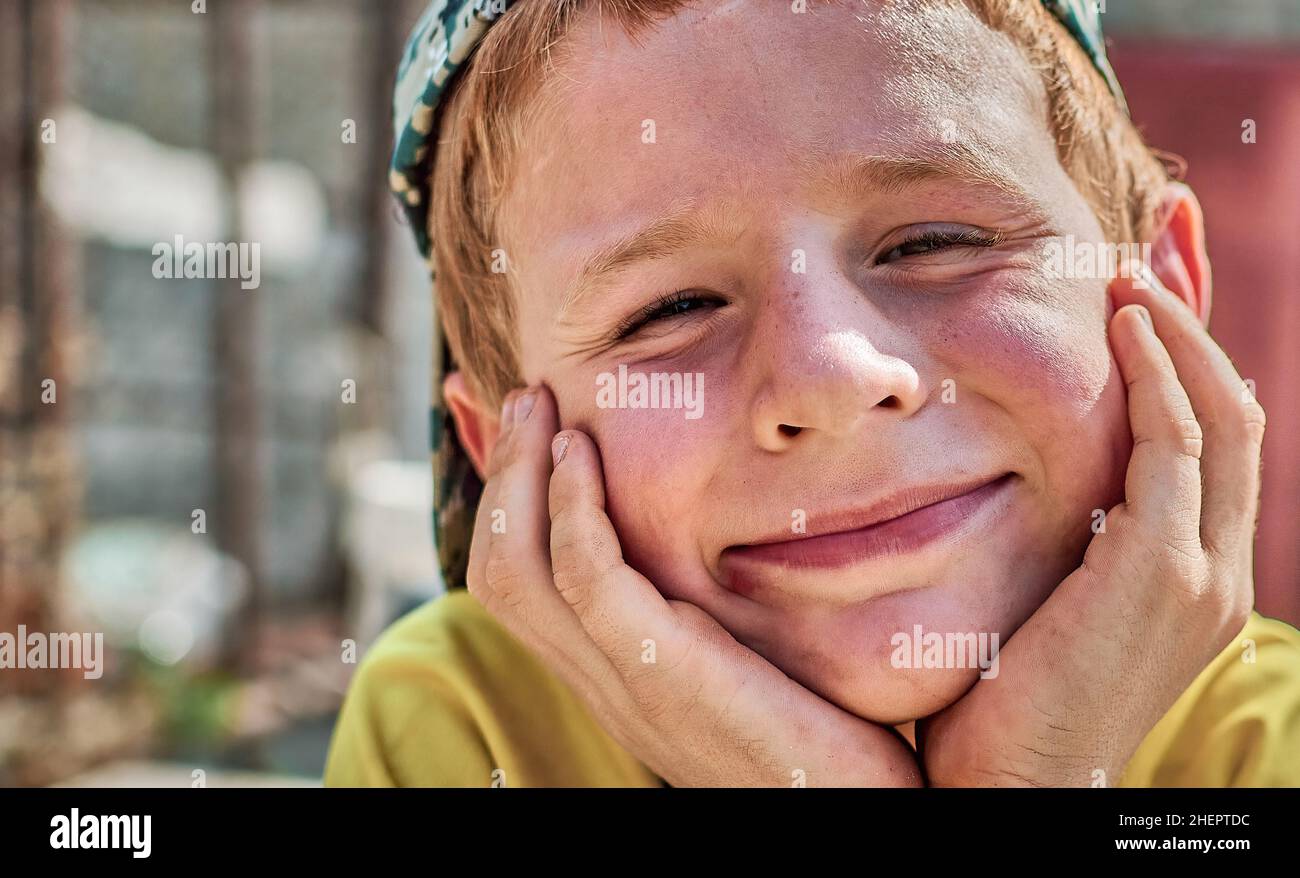Happy boy smiling with freckles and copper red hair holding hands on his cheeks  Stock Photo