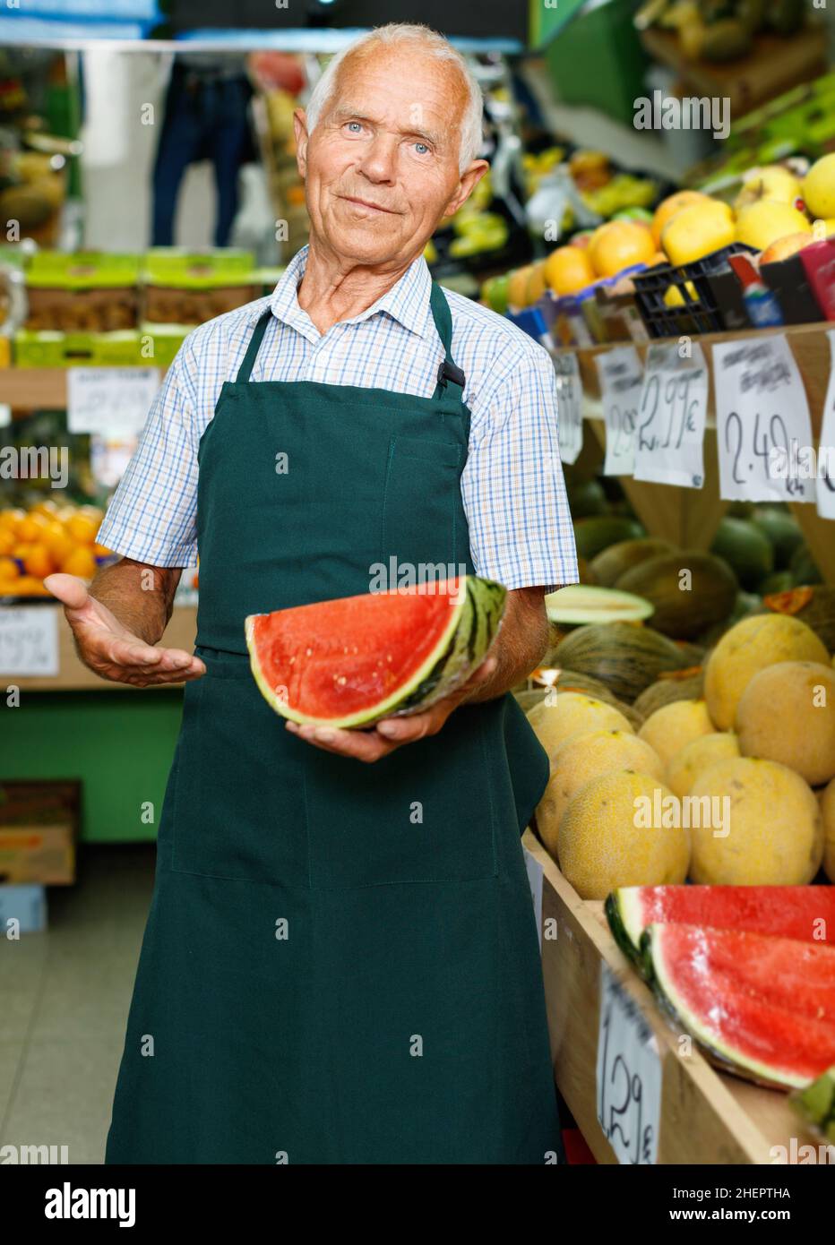 Positive senior male owner of greengrocery shop in apron offering fresh