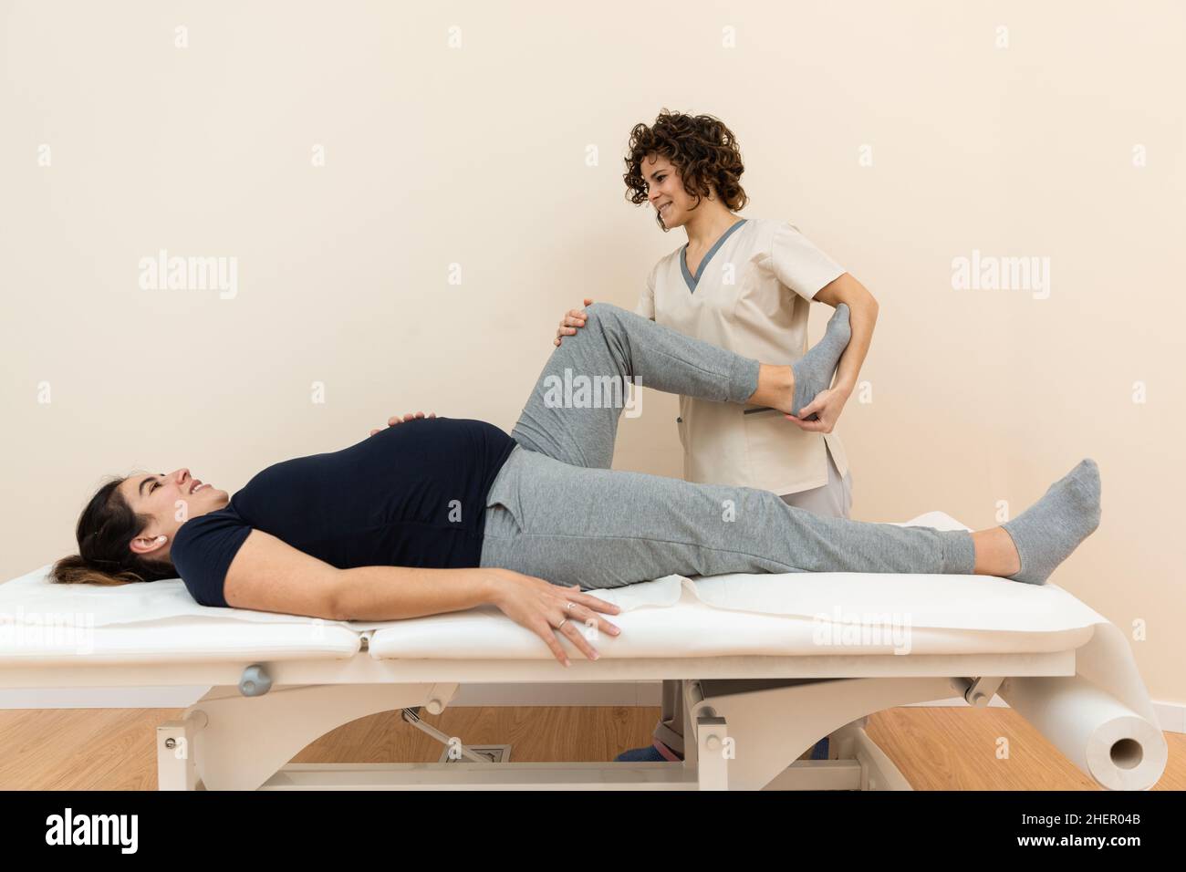 A pregnant woman lying on a massage table while a physiotherapist massages her legs at a health center Stock Photo
