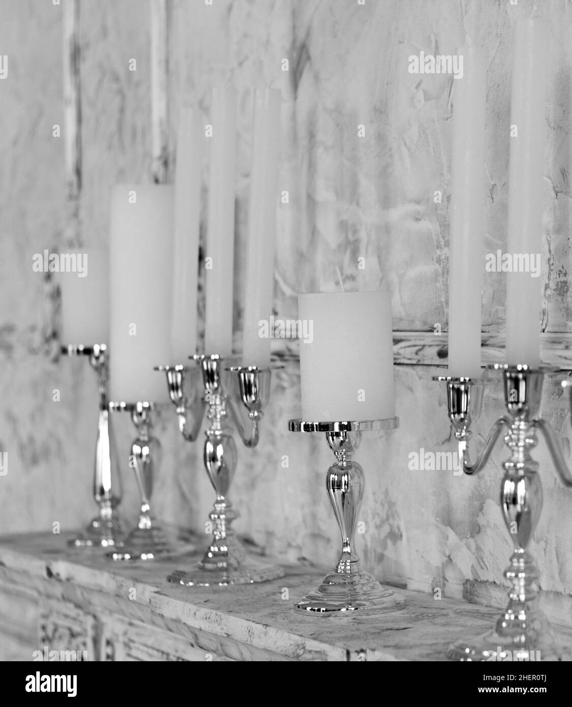 White candles in elegant candlesticks stand on a fireplace in the room Stock Photo