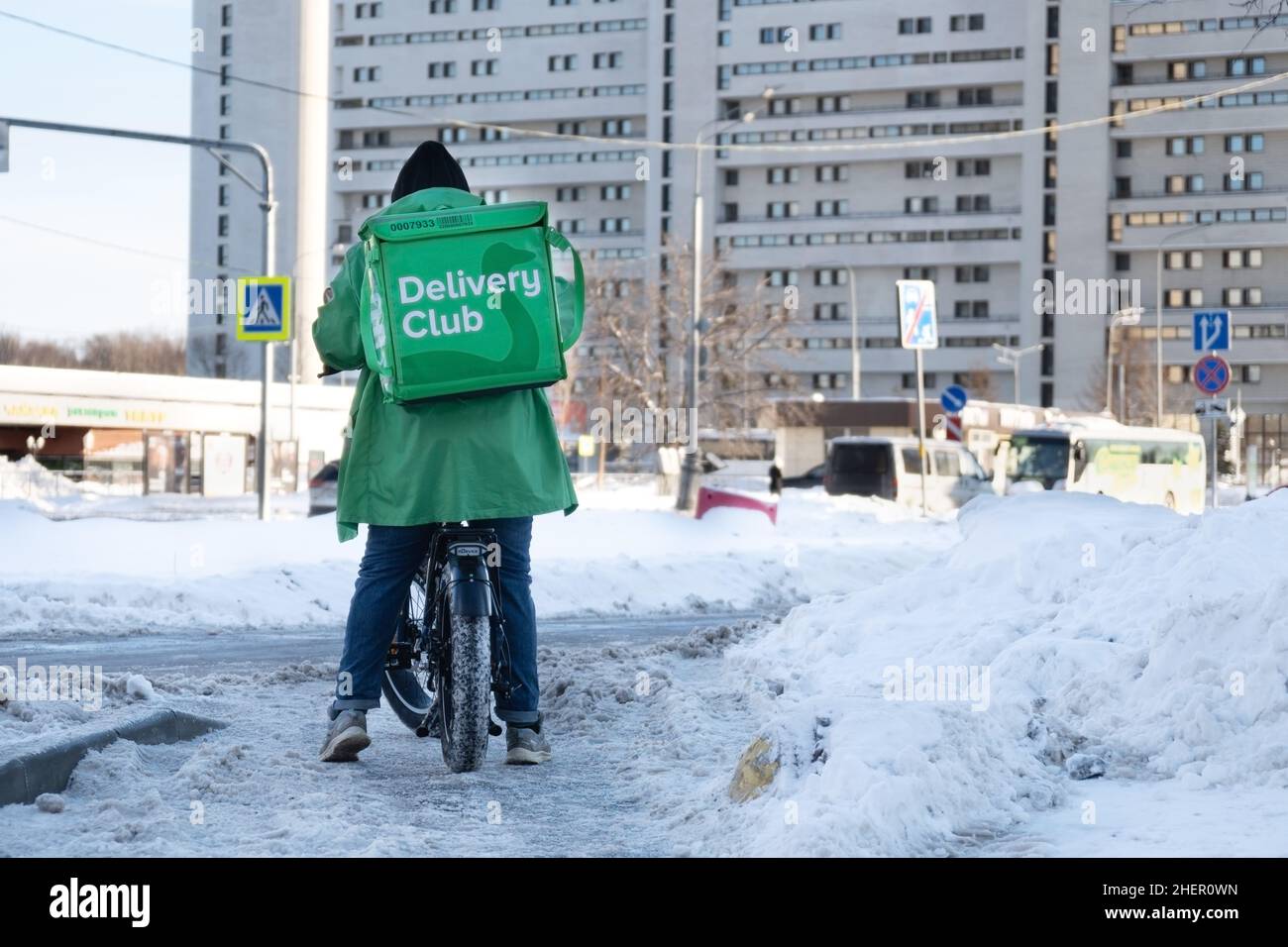 Moscow, Russia-January 7, 2022. Courier on bicycle with a large green backpack on the snowy Moscow street in cold winter day Stock Photo