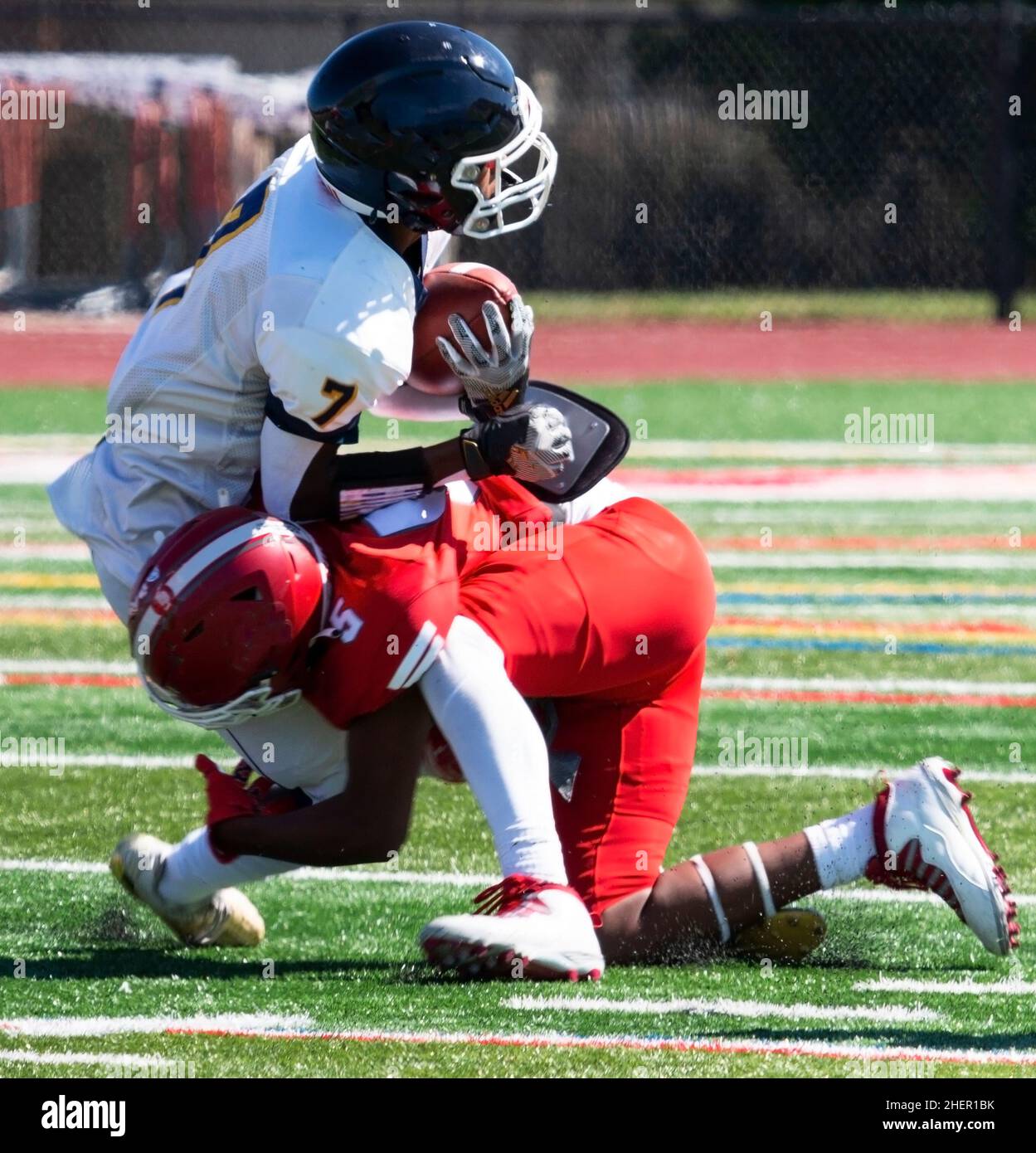 A high school football player tackling the opposing player on a turf field close up. Stock Photo