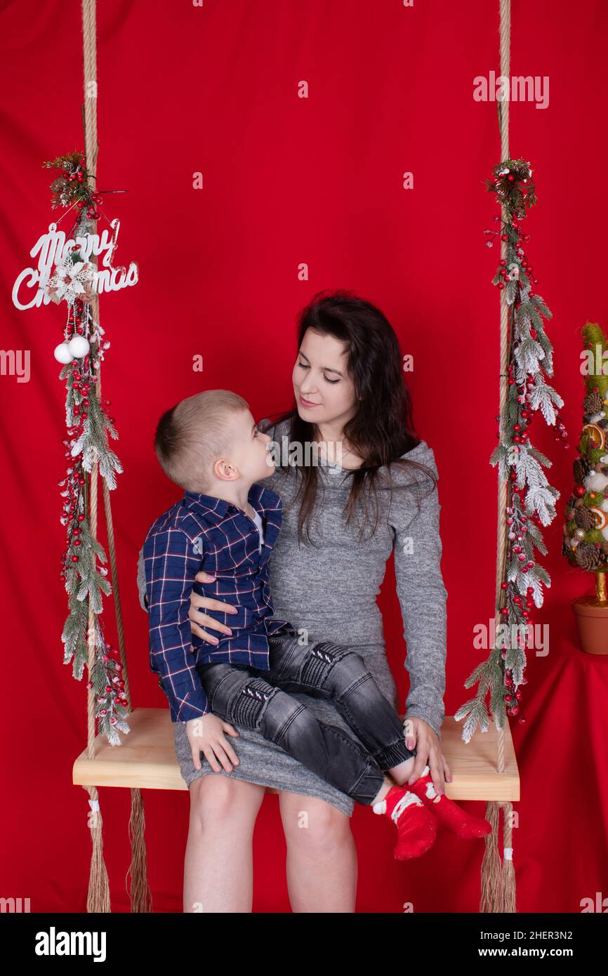 happy incomplete family hugging on wooden swing decorated with christmas  tree branches on red background. cozy young family. single mother in grey  dress and little baby son Stock Photo - Alamy