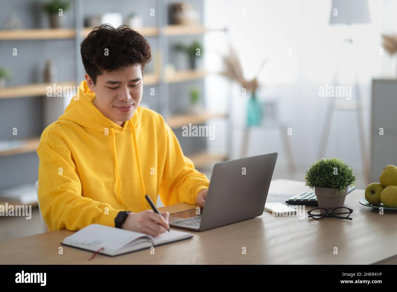 Asian man sitting at desk, using pc writing in notebook Stock Photo