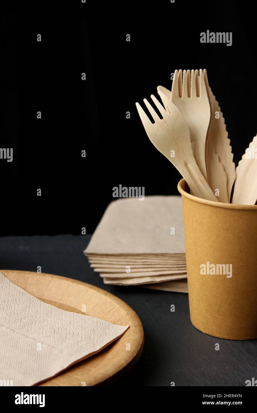Eco craft paper tableware. Paper cups, dishes and wooden cutlery on dark background. Recycling concept. Stock Photo