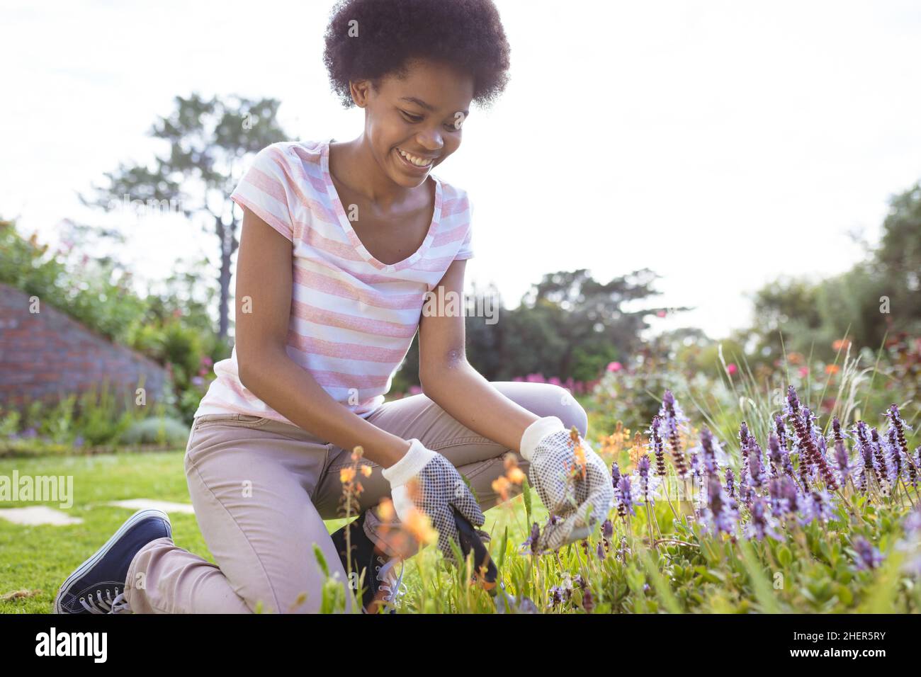 Happy african american teenage girl gardening in backyard on sunny day Stock Photo