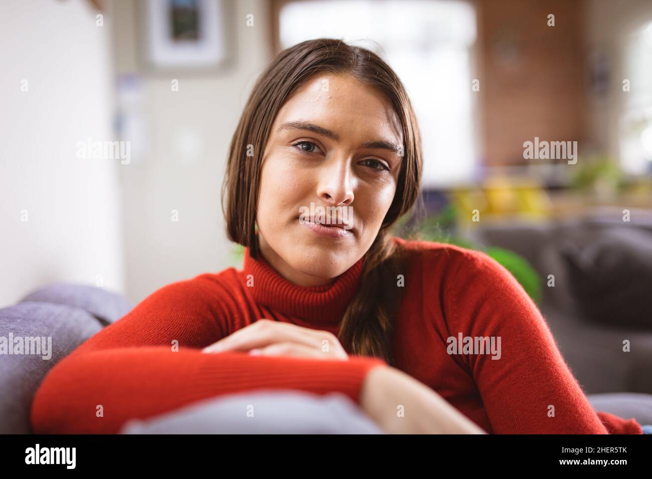 Portrait of beautiful young biracial woman with long brown hair sitting on sofa at home Stock Photo