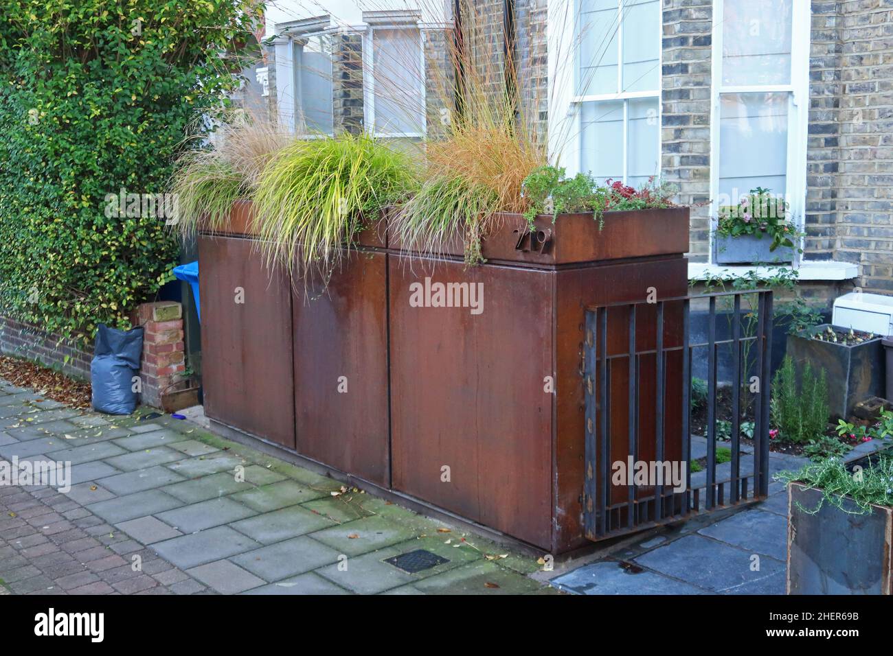 A corten rusty steel wheely-bin store on a Peckham street in London, UK. Houses council refuse bins and features a planting box on top. Stock Photo