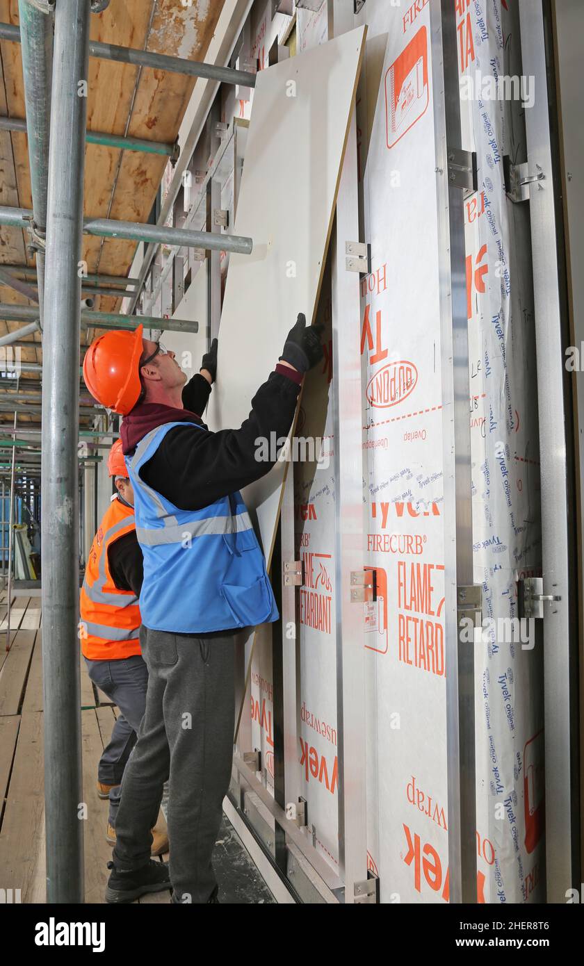 Workmen fix fire-resistant cladding panels and extra thermal insulation to the exterior wall of a London apartment block during refurbishment work Stock Photo