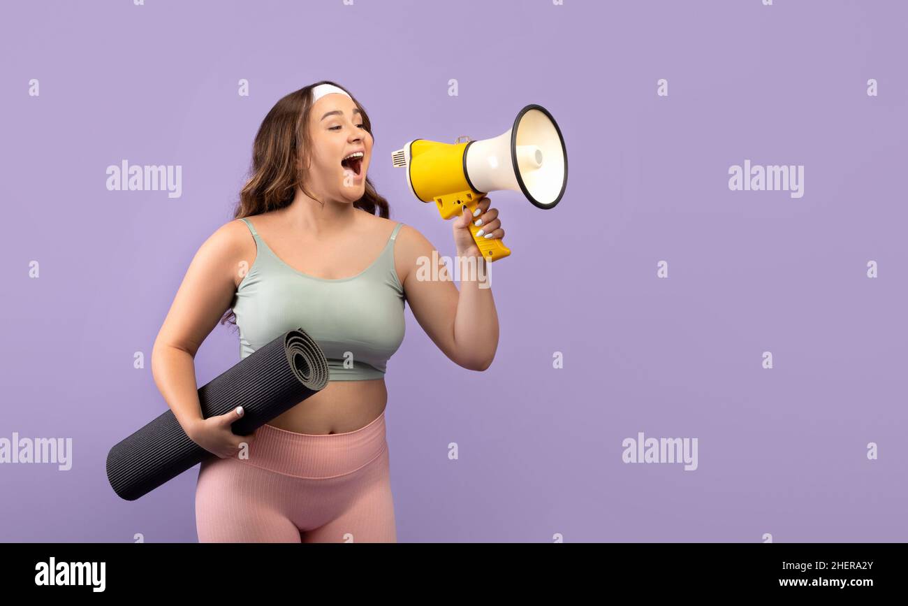 Funny millennial caucasian lady plus size in sports uniform with mat screaming at megaphone at free space Stock Photo
