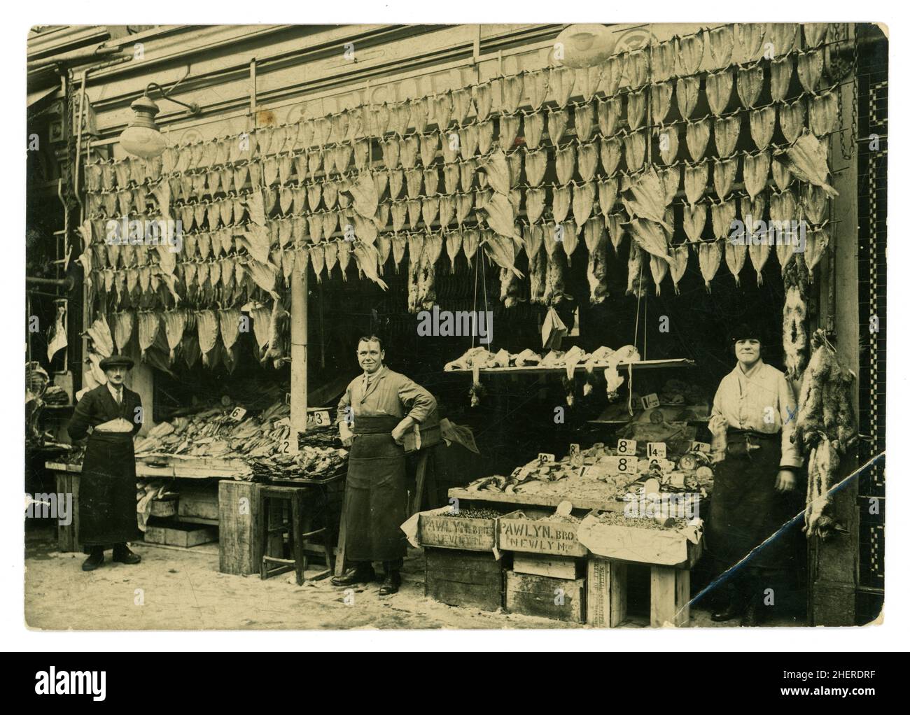 Original early 1900's, WW1 era photo of fishmongers, fish fillets hanging up in front of shop, crates of shellfish from Newyln, Cornwall, on display in wood crates at front of stall at a location in the Lavender Hill area of London, U.K. circa 1914-1918. Stock Photo