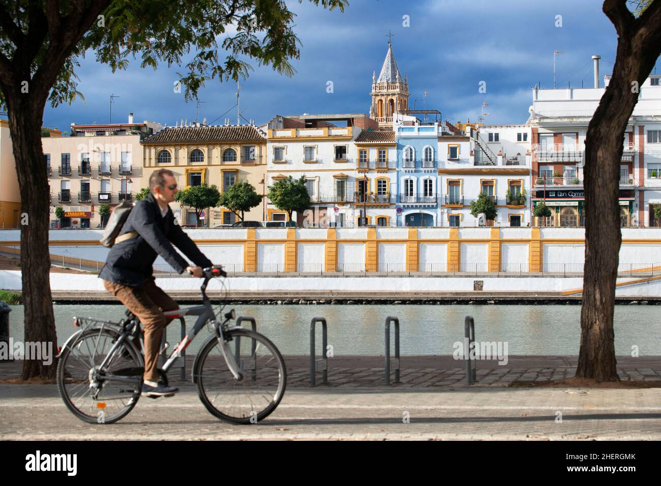Cyclists riding along the banks of the Guadalquivir River. Back front view of houses and apartments in the Triana barrio quarter of Seville - Sevilla Stock Photo