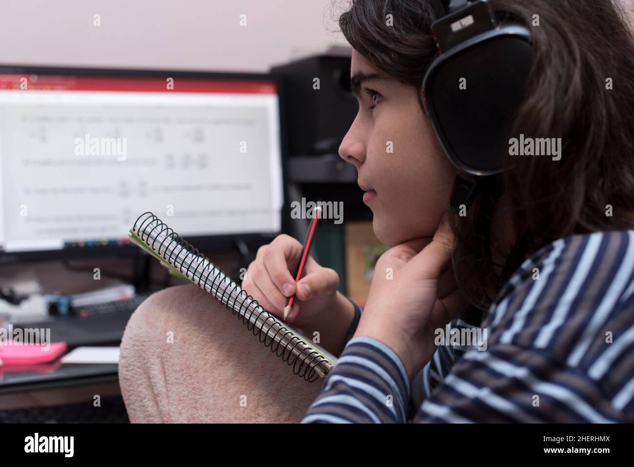 Transgender teenager with headphones and microphone studying in front of computer, watches a video of his tutor to solve math homework, while touching Stock Photo