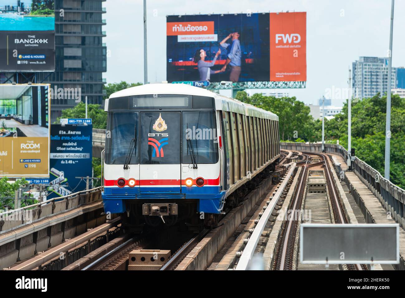 BTS Skytrain arriving at Saphan Taksin station in Bangkok. Large advertising boards in the background. Stock Photo