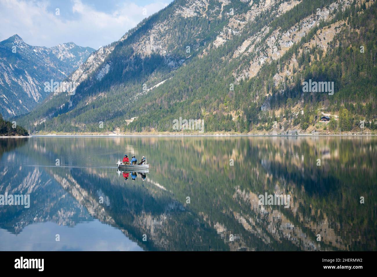 fisher boat at calm lake plansee with mountain reflections in spring ...