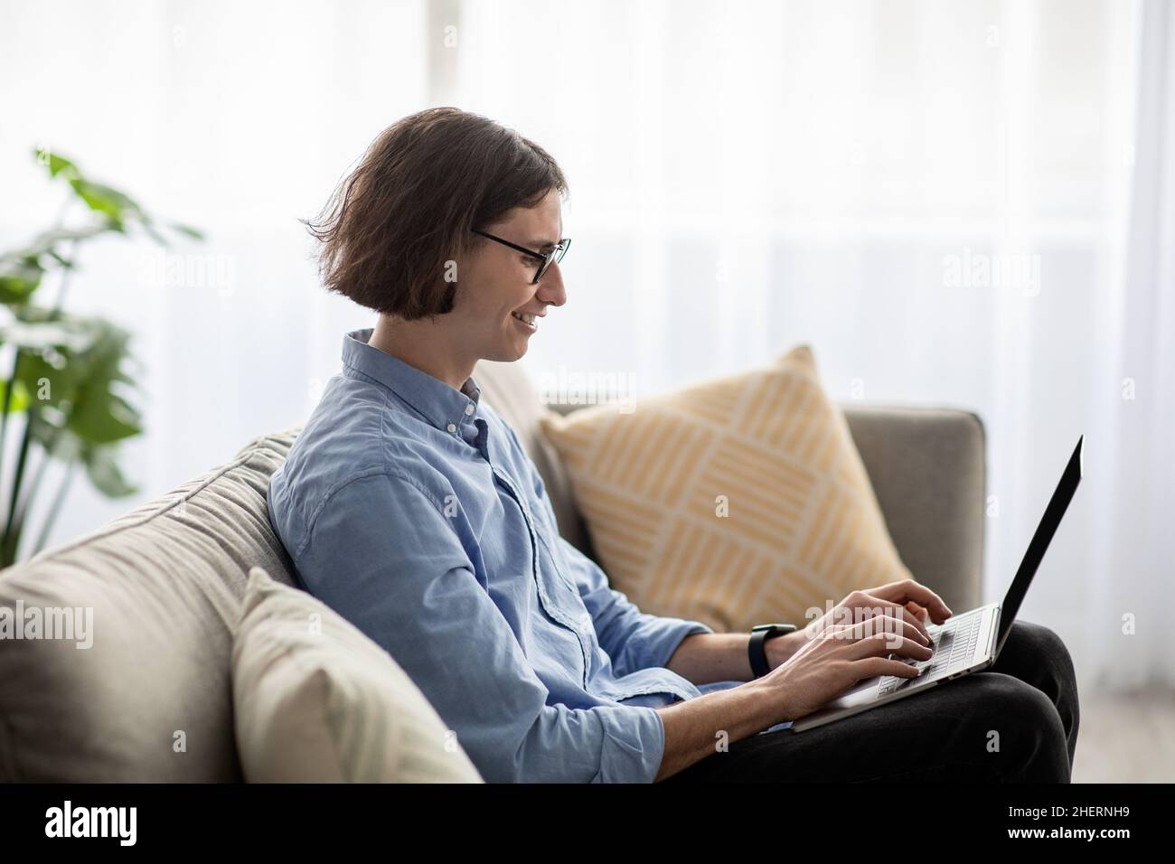 Handsome freelancer guy relaxing on sofa with laptop, enjoying domestic pastime and remote job opportunities, free space Stock Photo