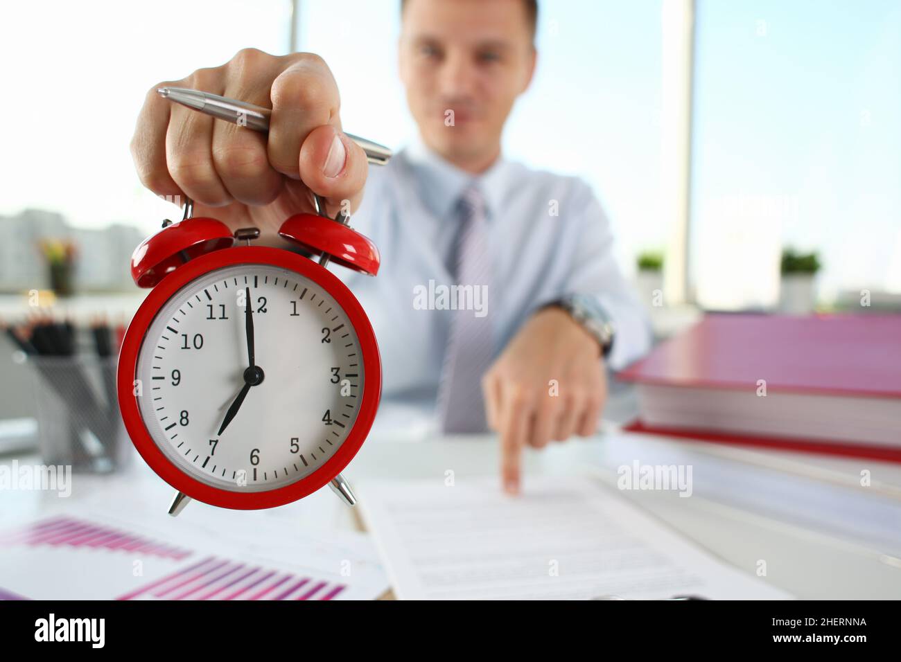 Man hand on red alarm clock stands at desk in office showing seven o