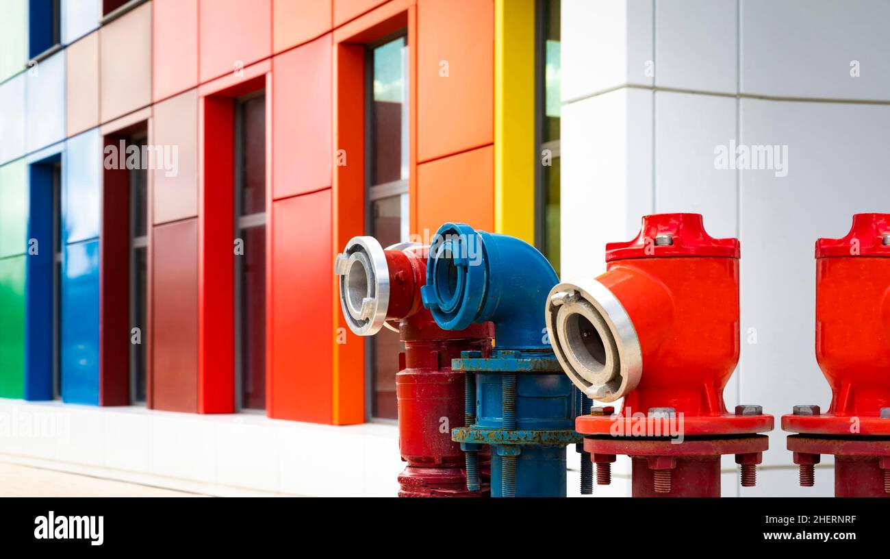 Colored hydrants with colored building in background, hydrants and multi-colored building, close up of three colored hydrants Stock Photo