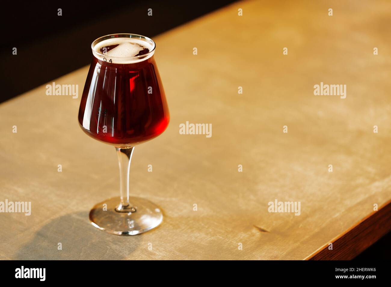 Glass with tasty red amber ale craft beer on table. Teku stemmed beer glass. Stock Photo