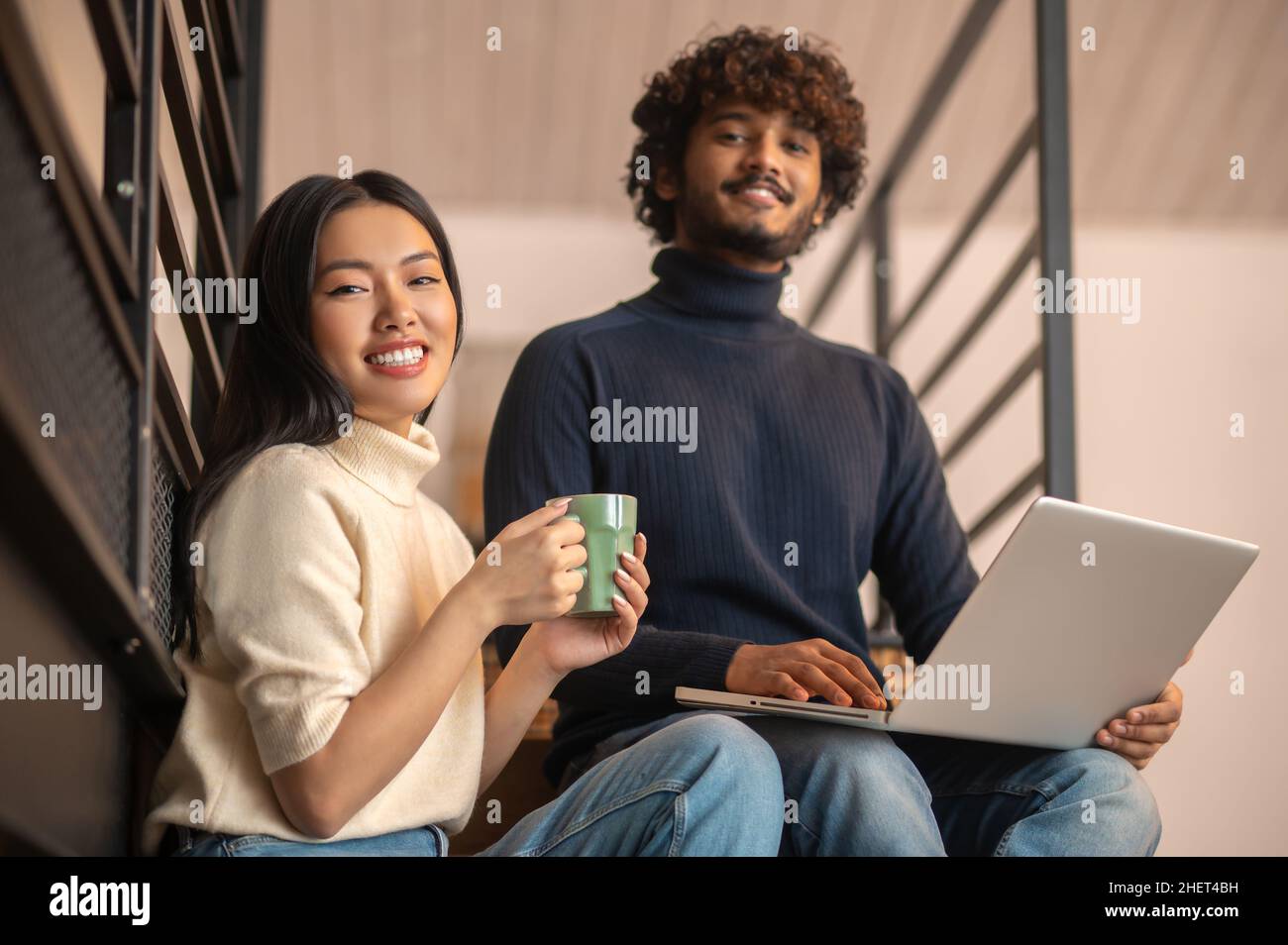 Woman with coffee man with laptop looking at camera Stock Photo