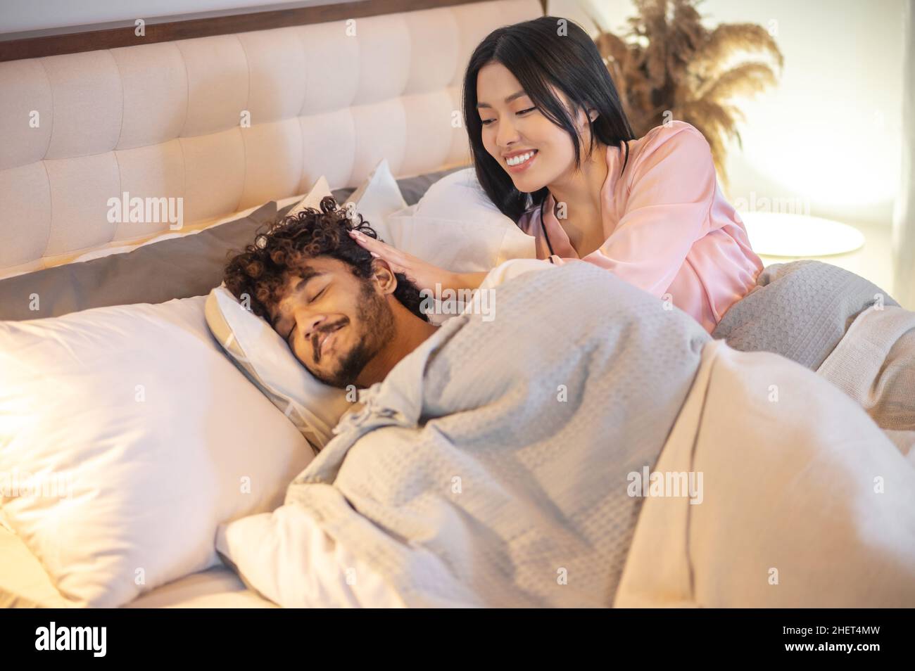 Woman touching mans head with closed eyes in bed Stock Photo
