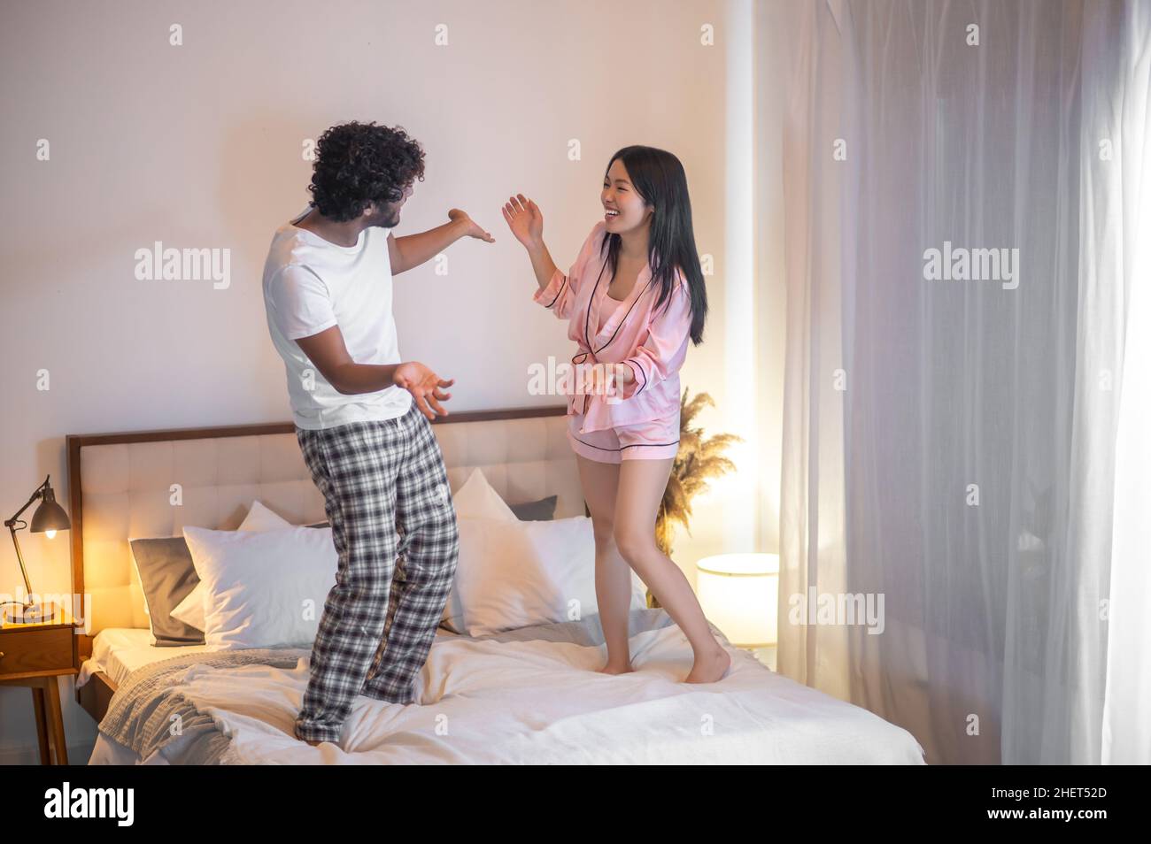 Woman and man standing on bed joyfully gesturing Stock Photo