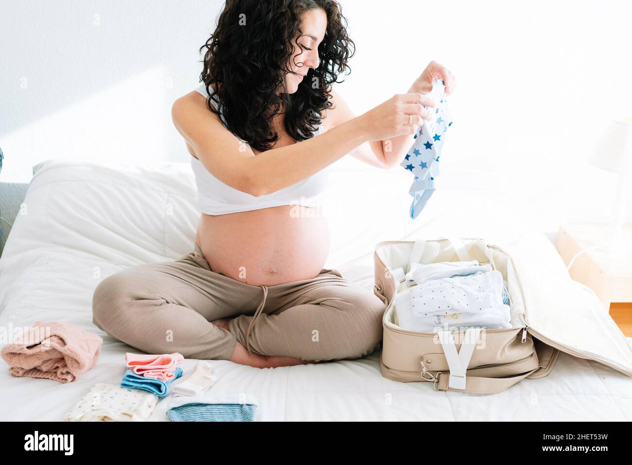 pregnant smiling young woman with curly hair preparing suitcase for hospital for the arrival of her newborn Stock Photo