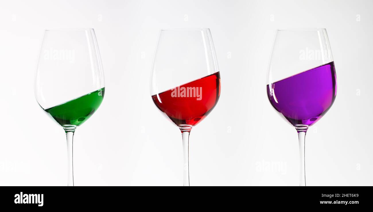 three green red and purple inclined filled wine glasses Stock Photo