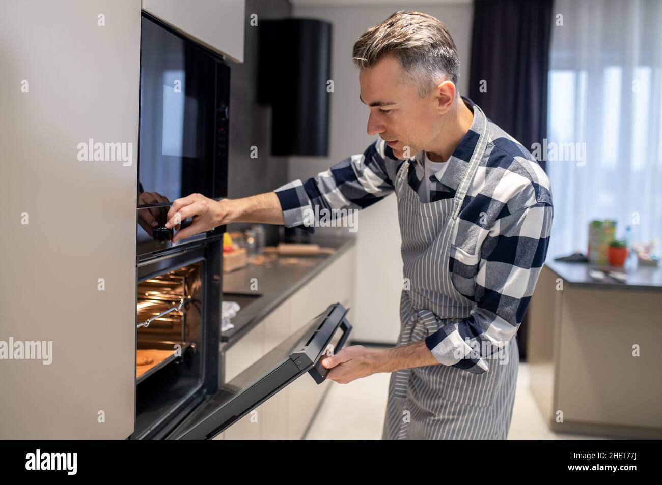 Man closing oven turning on regulating temperature Stock Photo