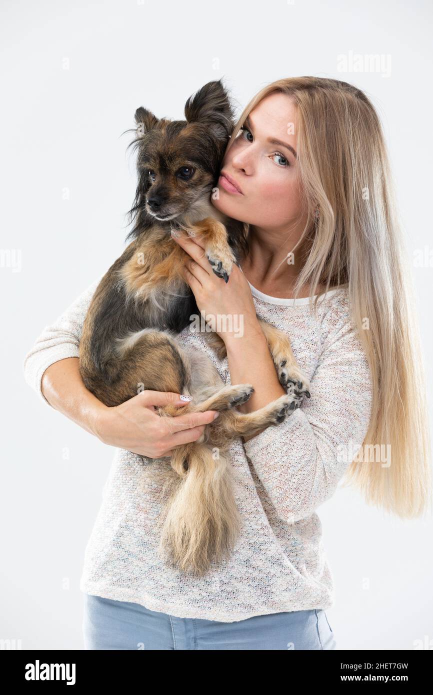 A blonde woman with long hair holds a small dog in her arms and looks at  it. Multi-breed dog Stock Photo - Alamy