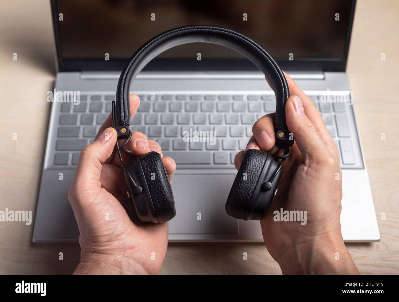 Headphones in hands and laptop. Listening to music and podcast concept. Stock Photo