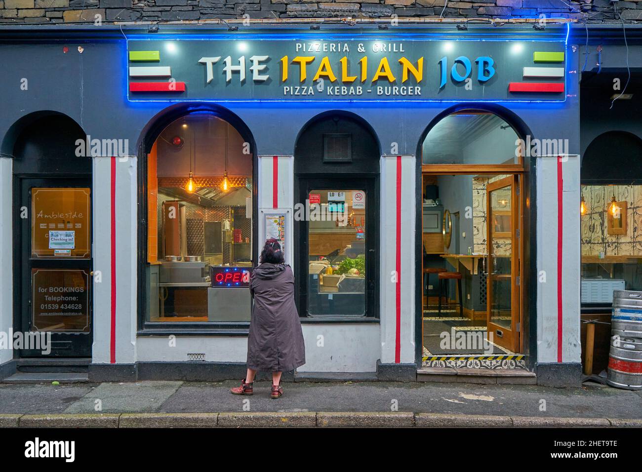 Façade of the colourful Italian Job pizzeria and grill in the town of Ambleside, Cumbria with a lone female standing in front examining the menu Stock Photo
