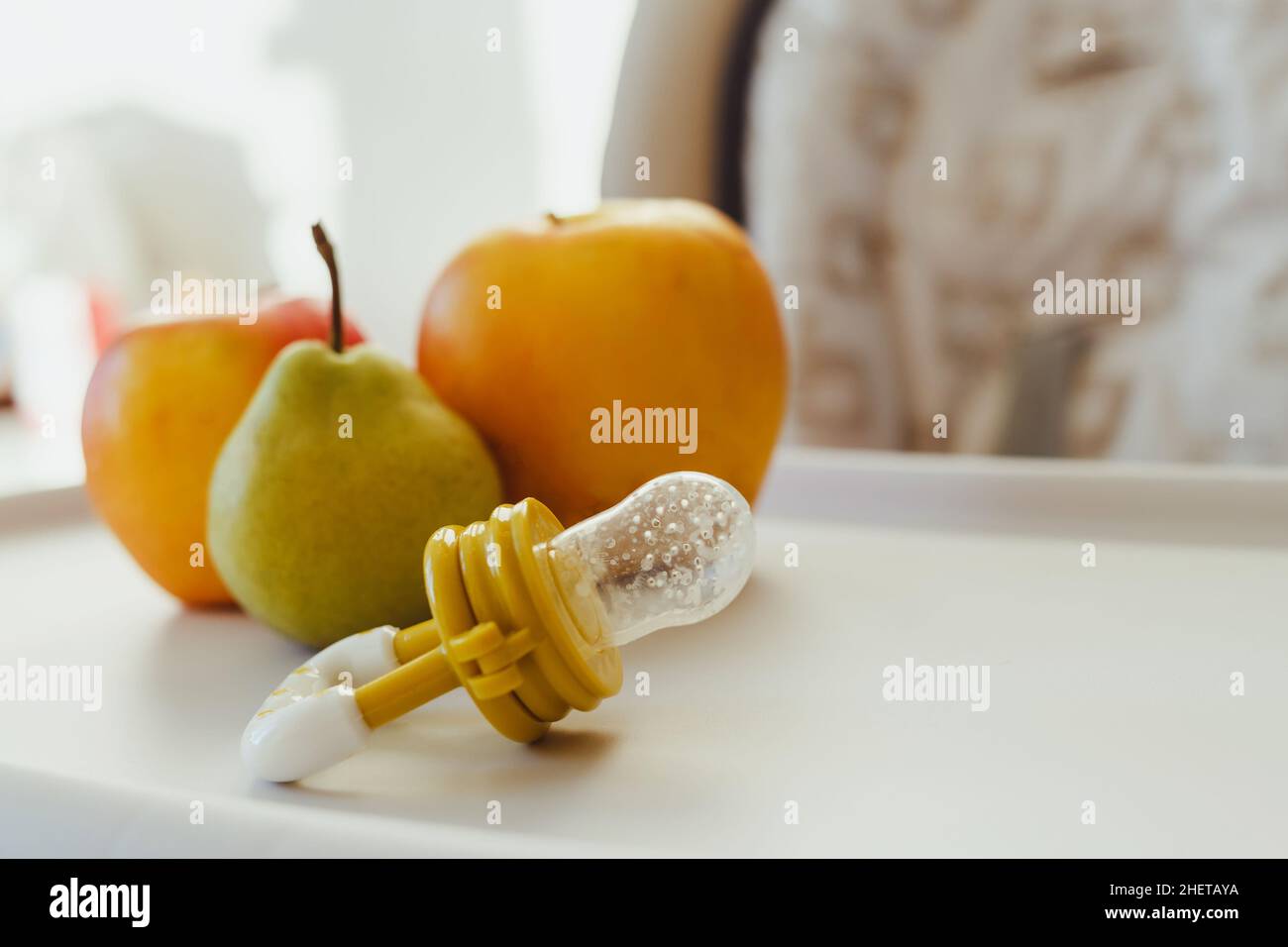 Nibbler with fresh apples and pear on light kids table, closeup. Baby feeder. Stock Photo