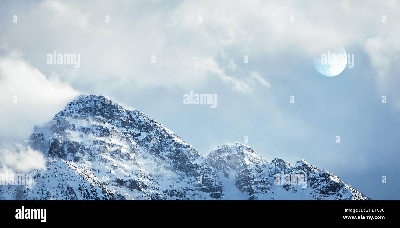 summit of snowy mountain with  fog and moon behind clouds Stock Photo