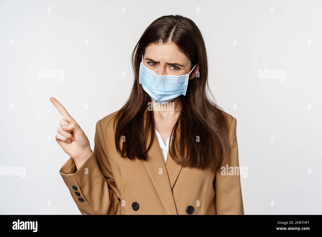 Coronavirus and people concept. Sad and concerned woman in office clothing  and medical face mask, sulking upset, pointing finger at upper left corner  Stock Photo - Alamy