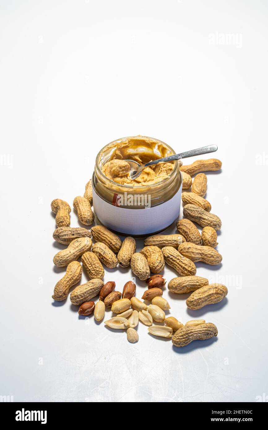 peanut butter in an open glass on a white background, next to scattered peanuts Stock Photo
