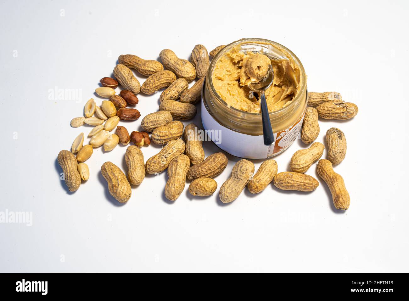 peanut butter in an open glass on a white background, next to scattered peanuts Stock Photo