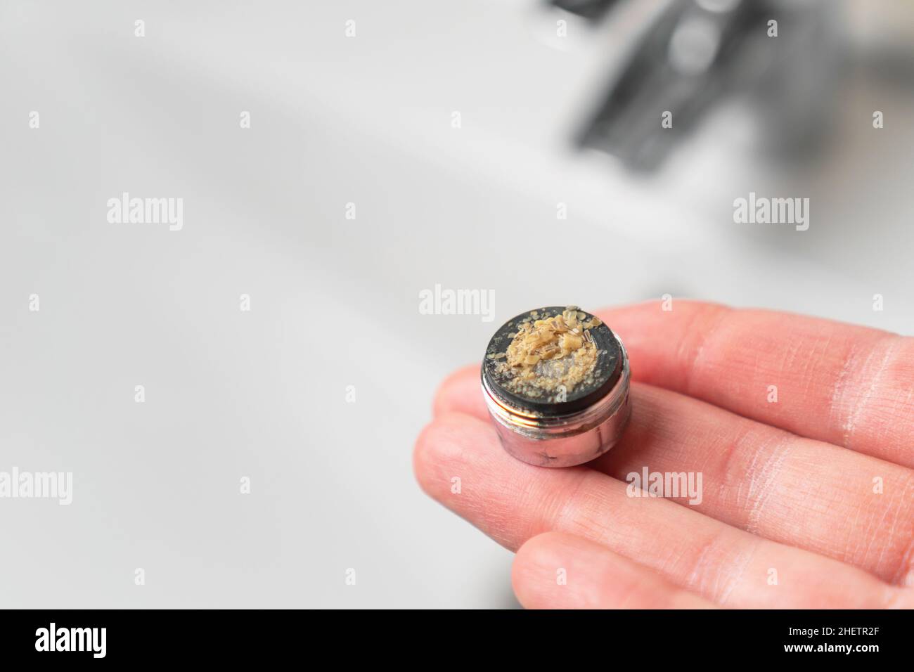 Dirty clogged bathroom faucet aerator in hand above the mixer in the