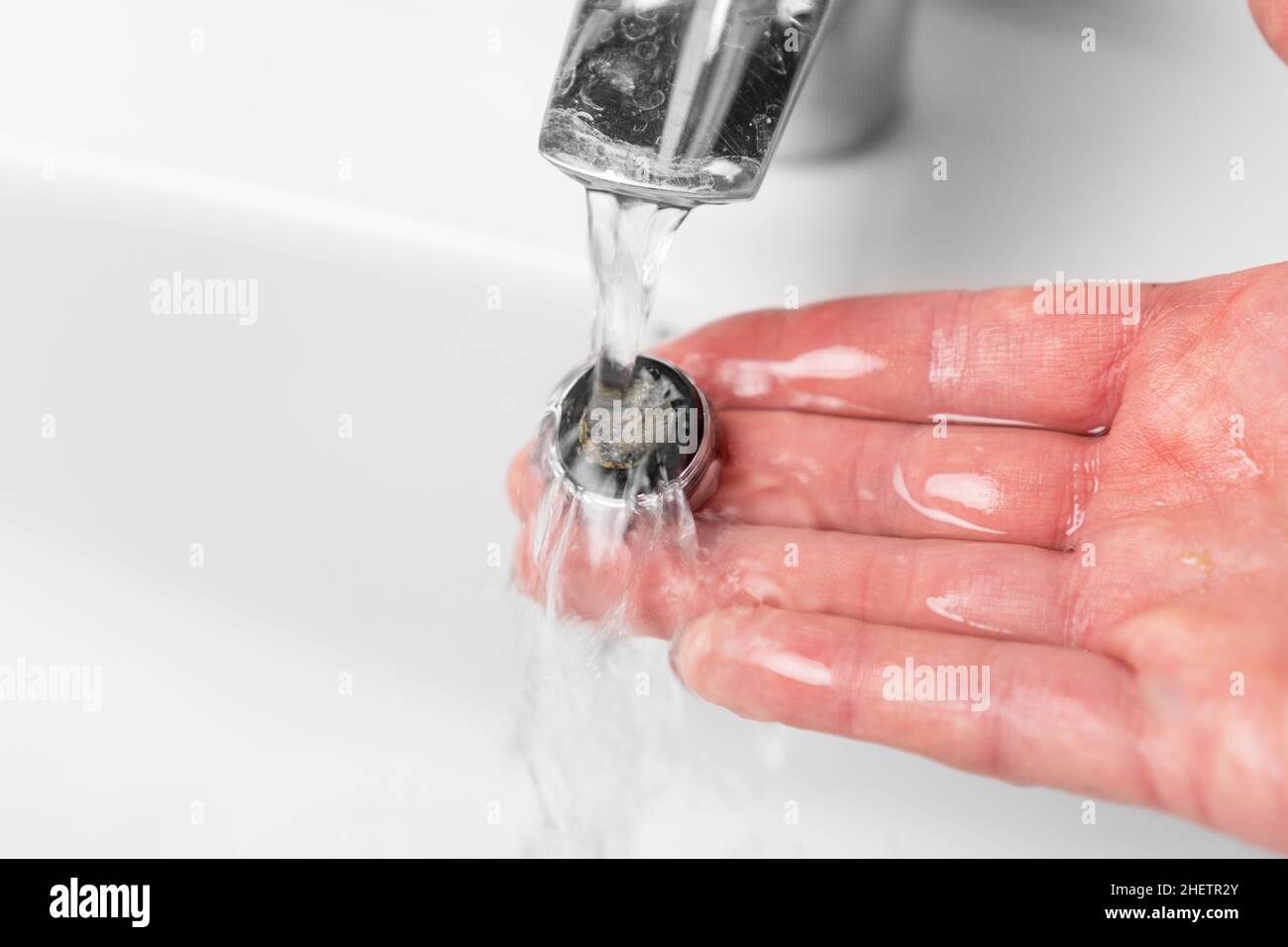 Washing the clogged filter aerator of a bathroom faucet sink with calcium sediments on the