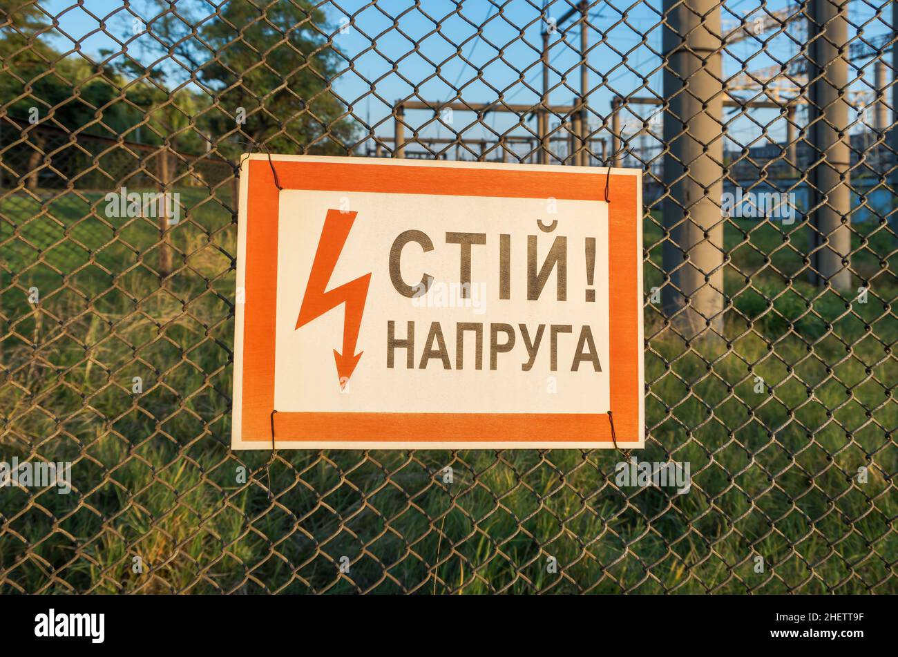 Warning sign - Stop! Voltage. There is chain-link of mesh fence. Inscription in Ukrainian - Stop! Voltage Stock Photo