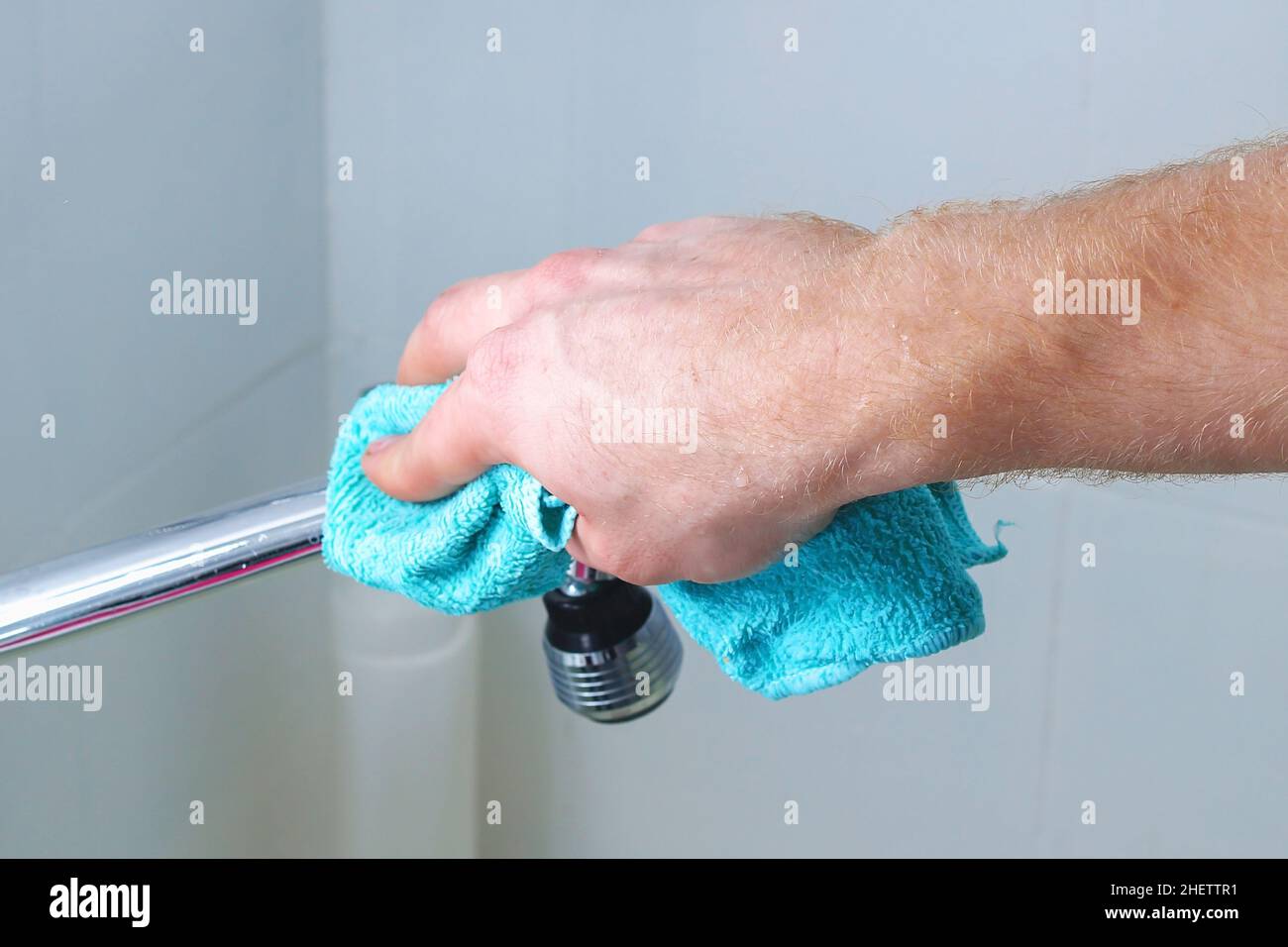 A man wipes a mixer tap, a faucet with a rag. Cleaning of the house ...