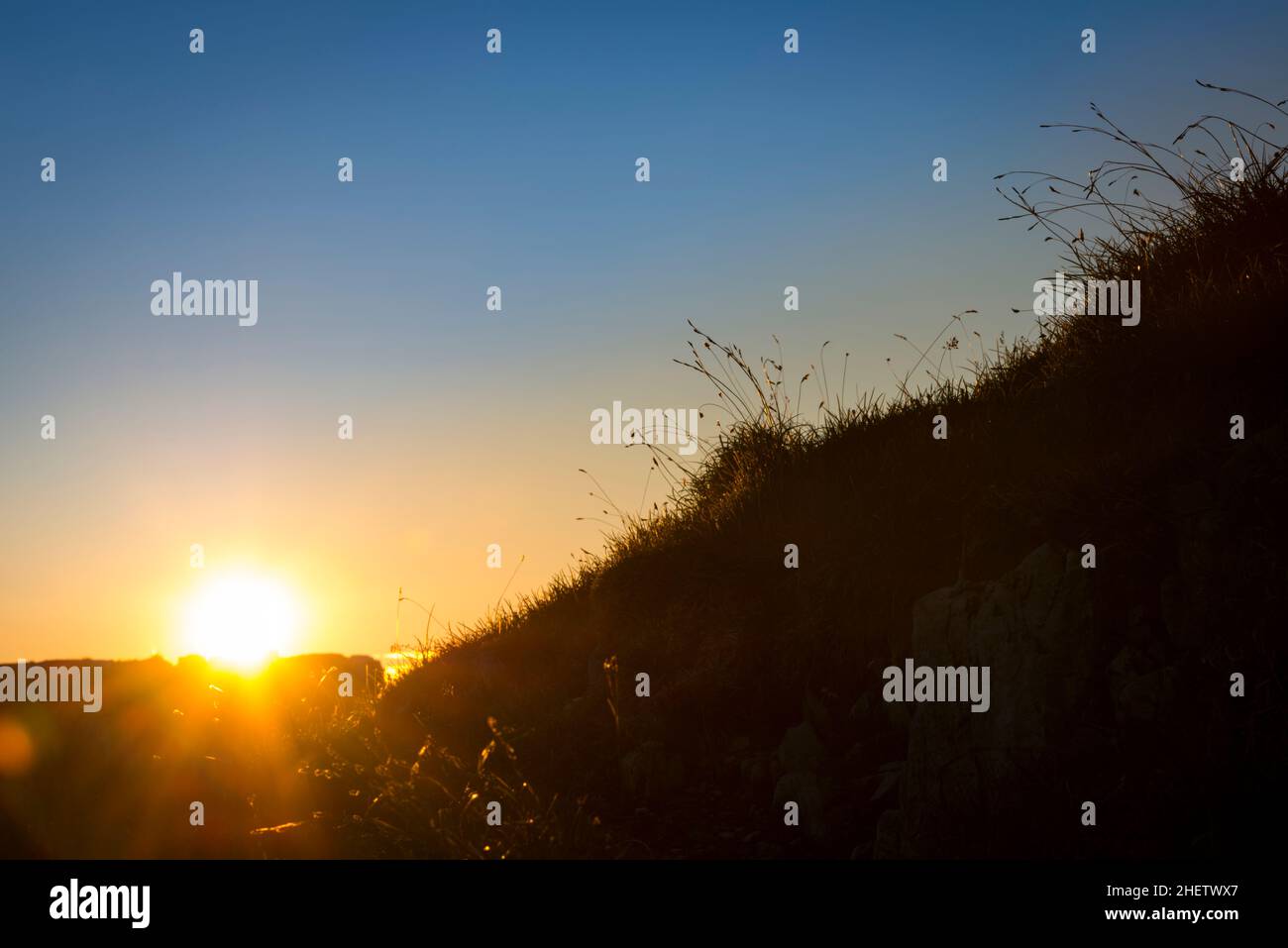 sun while sunset behind rock on mountain with grass silhouette Stock Photo