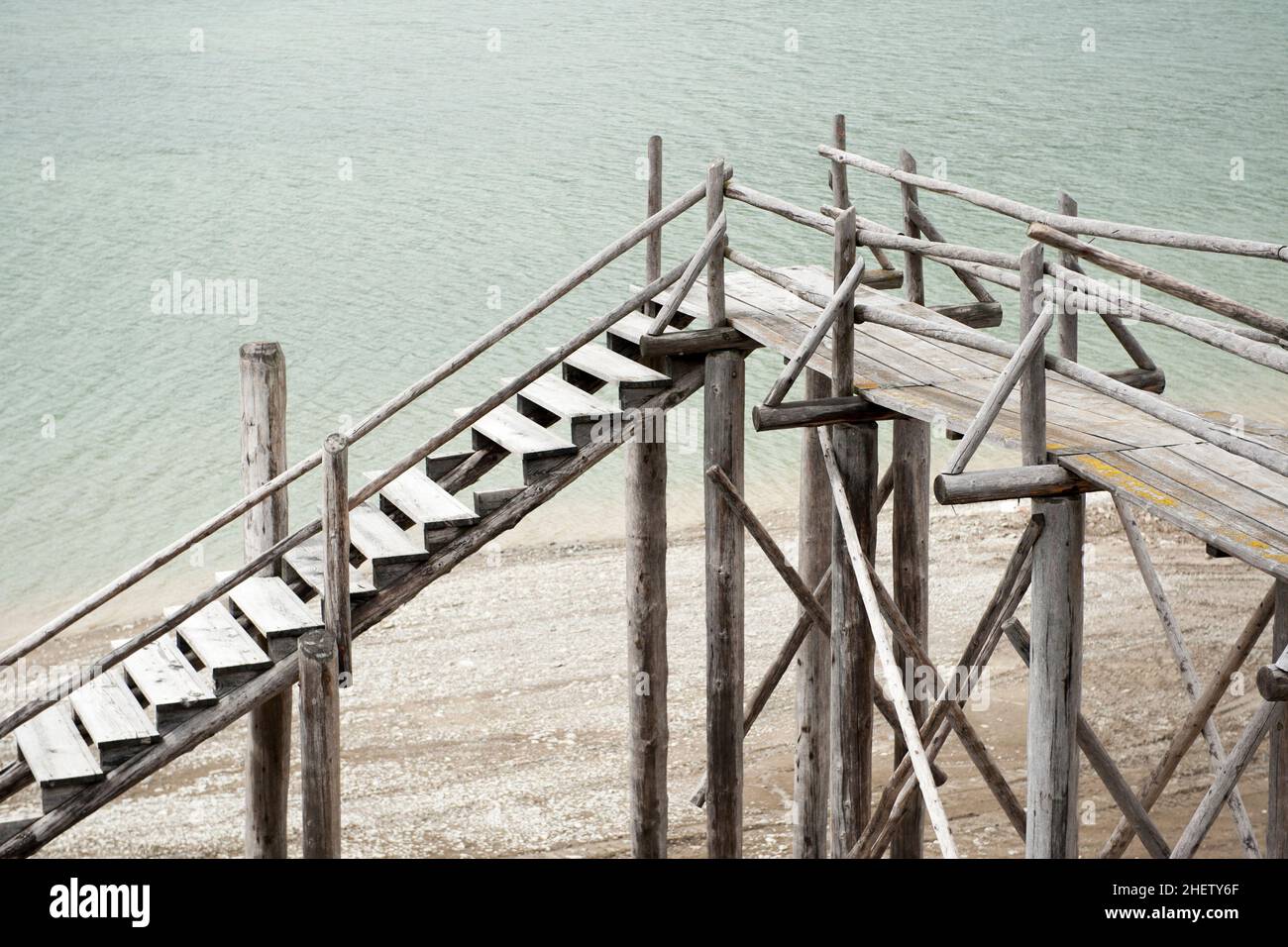 blocked obsolete wooden catwalk bridge at lake with less water and gravel at coast Stock Photo
