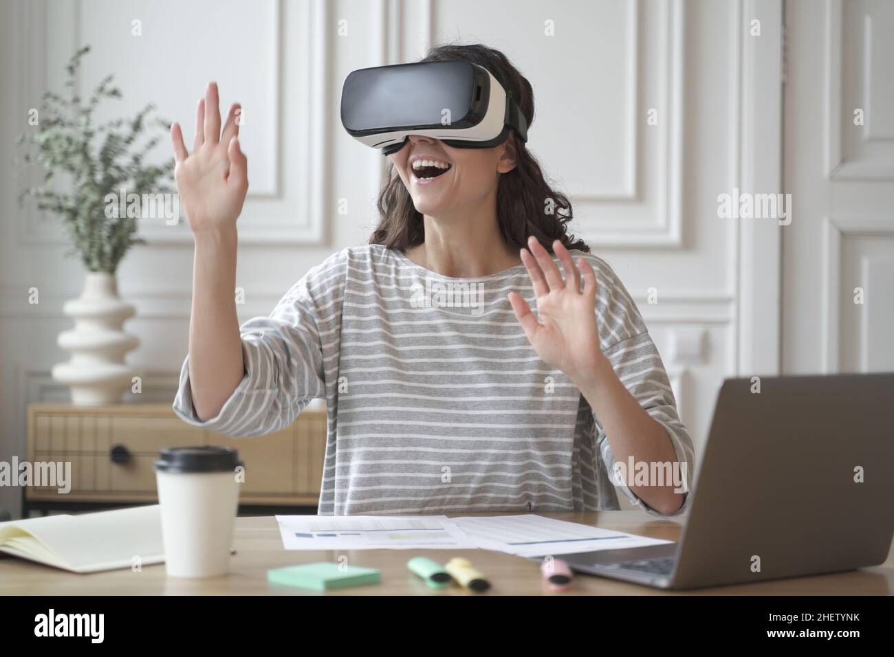 Excited amazed woman wearing VR glasses enjoying amazing virtual reality experience at work Stock Photo