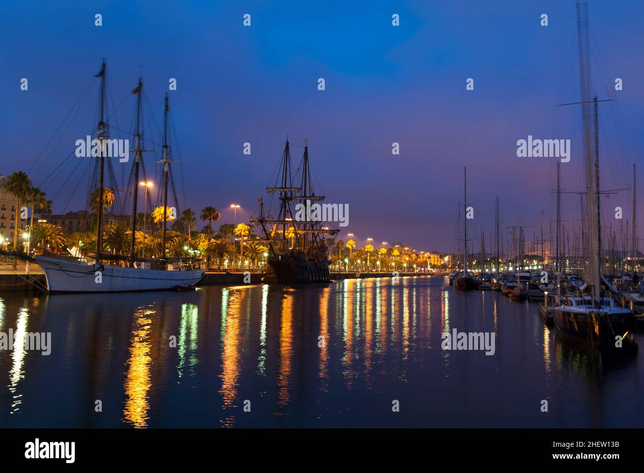 Nightscene with a rigged schooner and tall sailing ships in a peaceful calm harbour with colourful city lights from the waterfront reflected on the wa Stock Photo