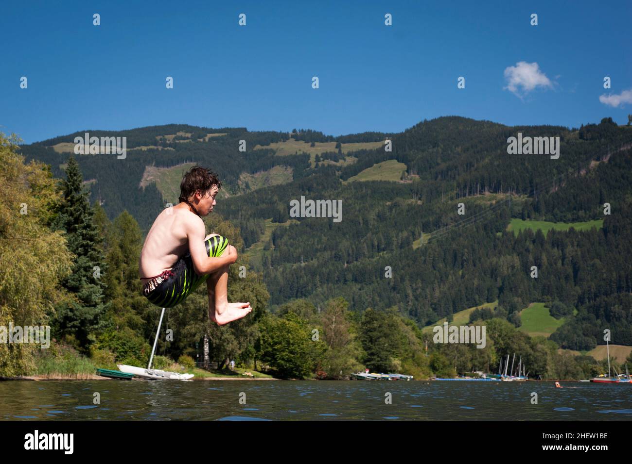 male teenager in the air while jumps in to a lake with nice nature in the back Stock Photo