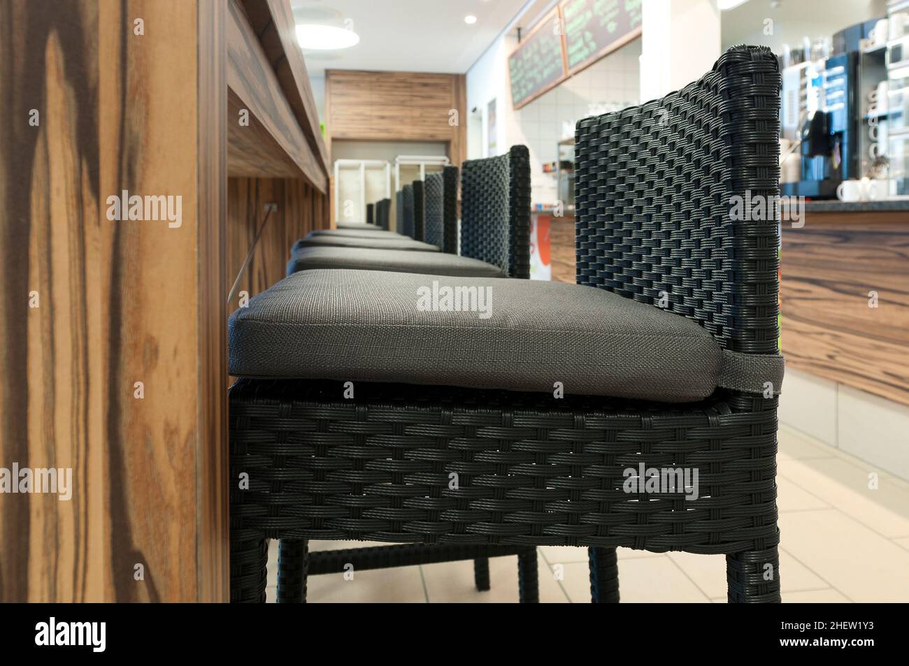 aligned high rattan chairs with  seat-contact surface in front of wooden table in self service restaurant Stock Photo