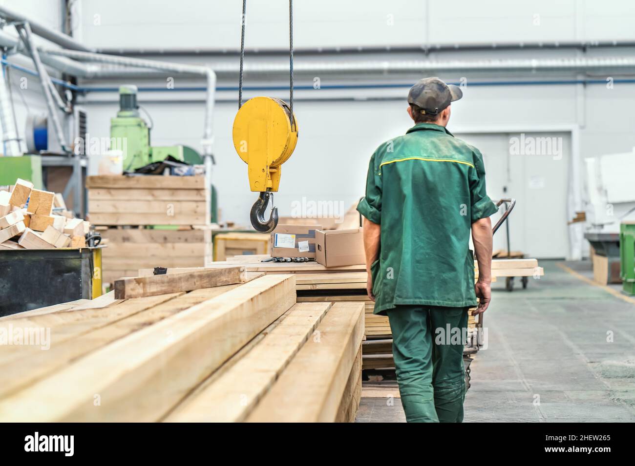 Worker in uniform in big industrial wood factory interior for furniture production, rear view. Stock Photo