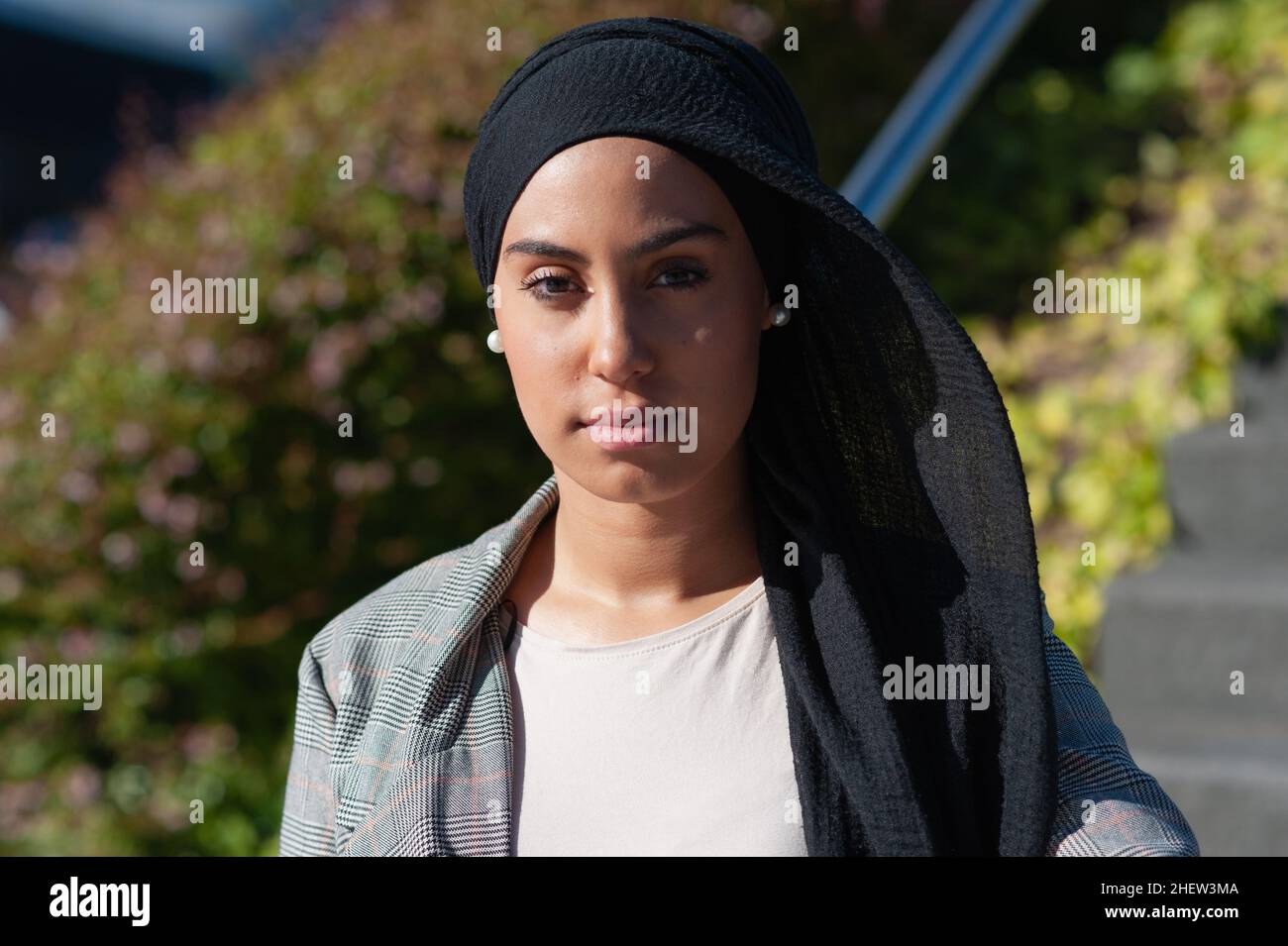 Portrait of an unsmiling muslim woman standing near park stairs looking at camera in a sunny day. Stock Photo