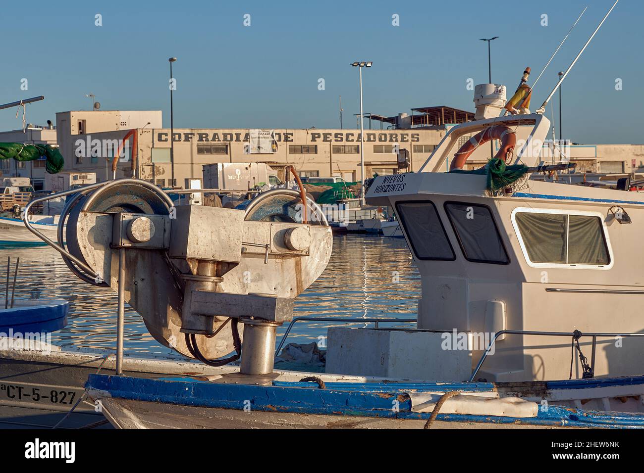 Fishing boat with pulleys to tow the nets in the port of Santa Pola and the building of the fishermen's brotherhood in the background, Alicante, Spain Stock Photo
